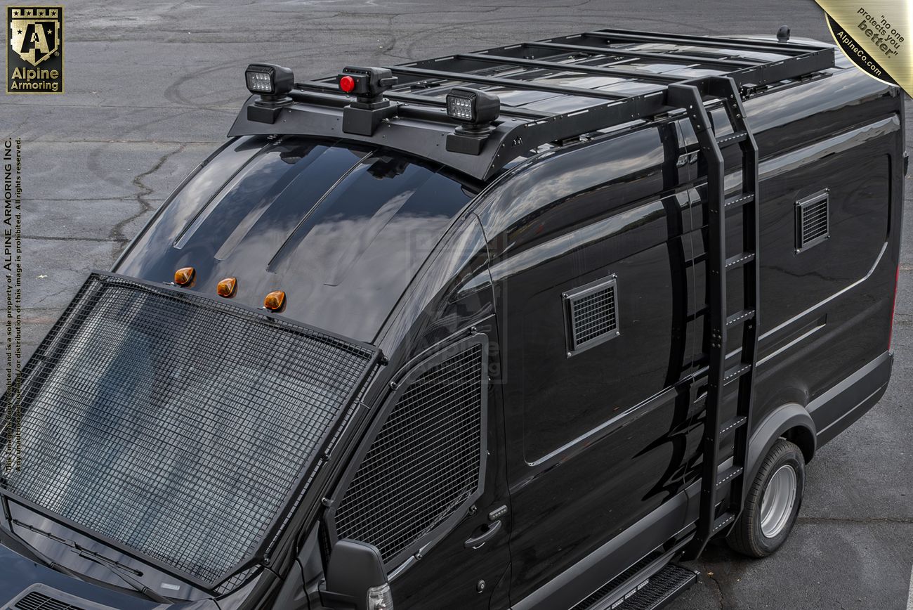 A view from above a black armored SWAT van, known as the Armored Pointer from Alpine Armoring, parked outdoors. The vehicle features reinforced windows, tactical lighting, and a robust build designed for law enforcement and high-risk operations.