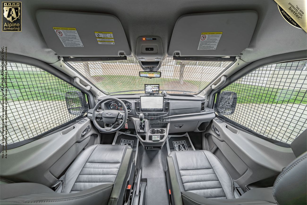 Interior view of a Pointer van's front cabin, featuring two seats, a control panel with a steering wheel, and a metal grid partition behind the seats.