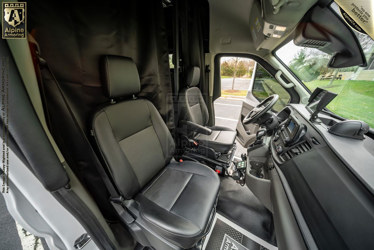The image shows the interior front cabin of a n armored Pointer van with two black seats, a steering wheel, dashboard, and a mounted navigation screen. A black curtain partially covers the driver's side area.