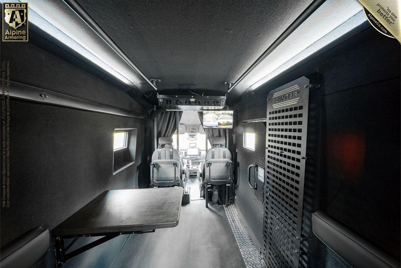 A black Pointer van with its rear doors open, revealing organized interior equipment. The van is parked on a paved surface with green foliage in the background.