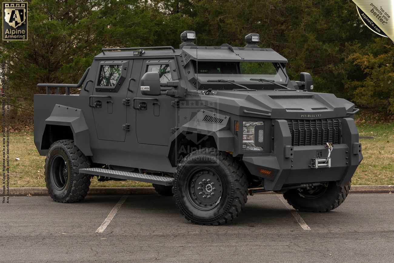 A heavily armored, matte black Pit-Bull VXT designed for tactical operations, parked in an outdoor setting with trees in the background.