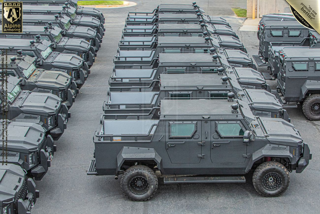 Rows of identical Pit-Bull VXT vehicles are parked in an orderly formation in an outdoor lot marked with the Alpine Armoring logo.