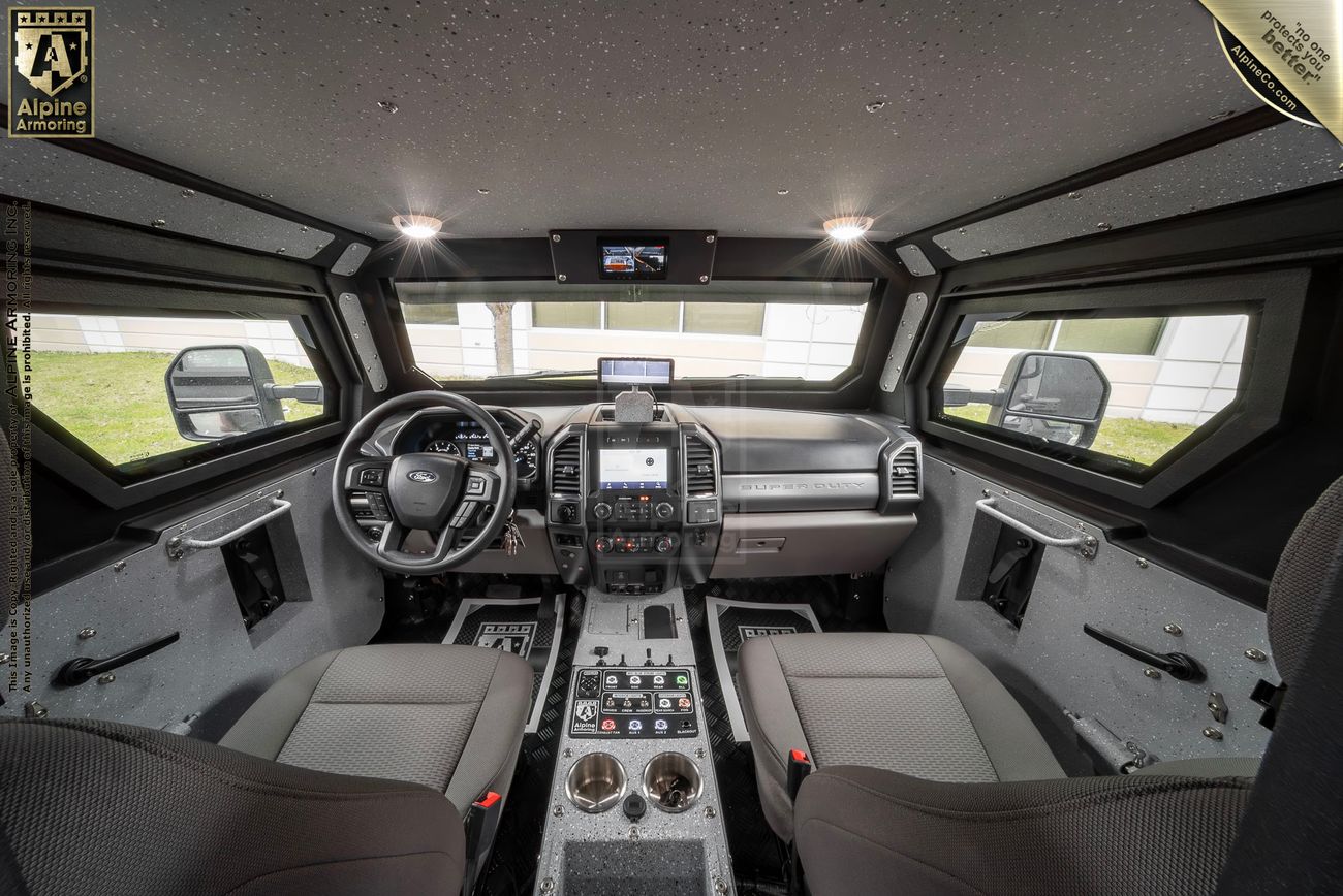 The interior of a high-tech Pit-Bull VXT cockpit with two seats, multiple screens, control panels, and various buttons. The view from the windshield shows a building and a lawn outside.