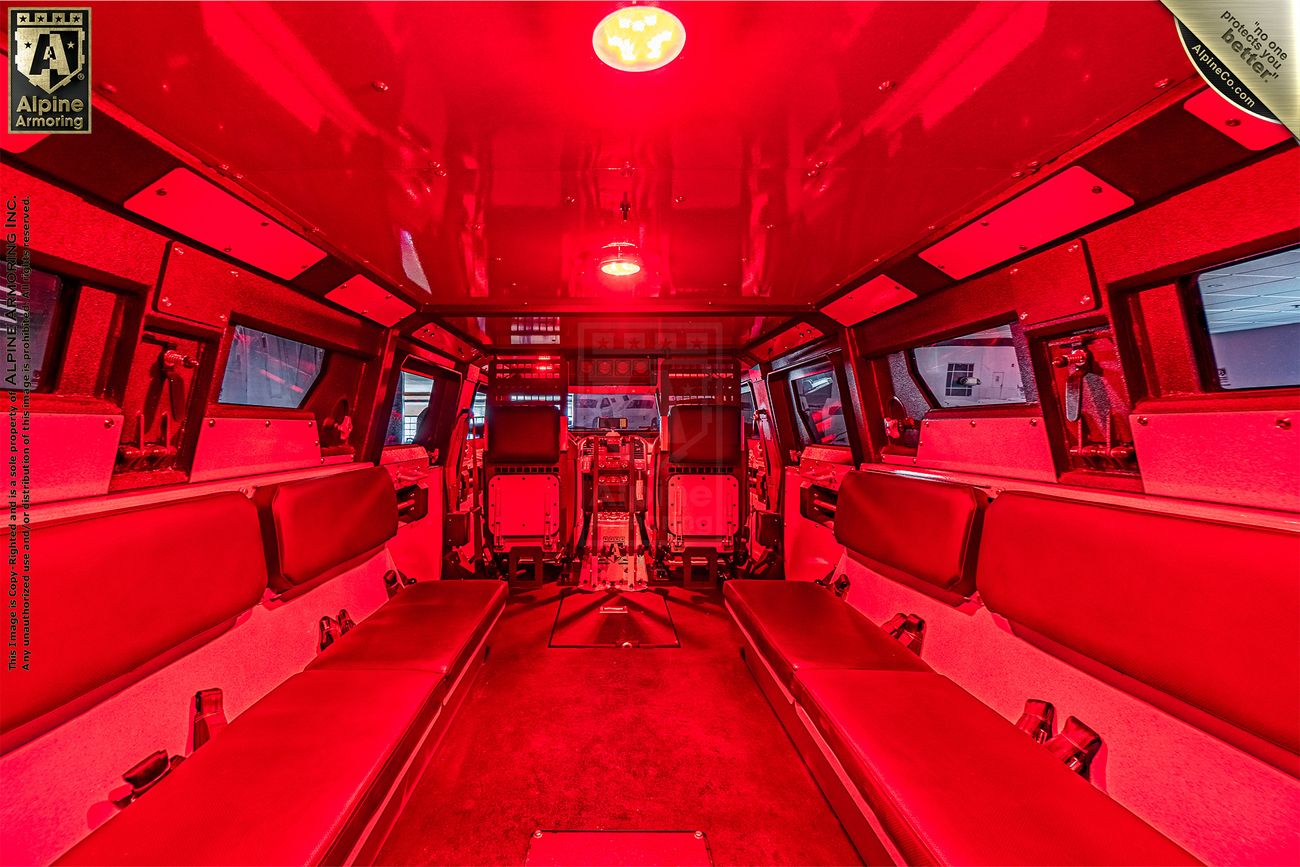 Interior of a armored Pit-Bull VX APC vehicle with red lighting showcasing rows of seats along both sides, designed likely for transporting multiple passengers or personnel.